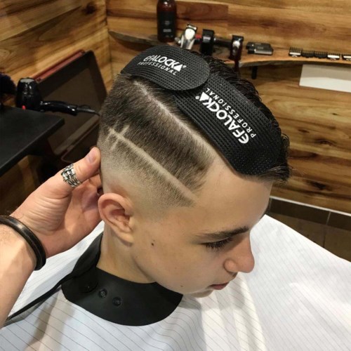 Young man with a modern, stylish haircut, featuring shaved sides and a patterned design. He wears a protective headgear.
