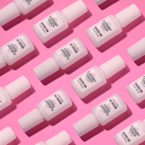 Multiple small white bottles with black text, labeled 'Elegant Touch Big Brush On'. They're arranged in rows on a pink background.