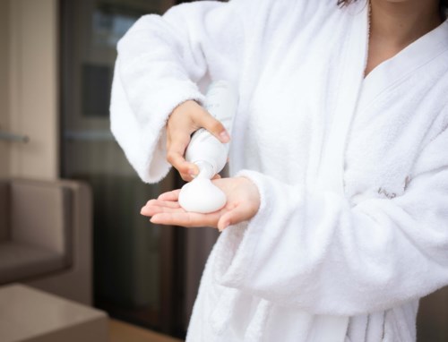 Person in a white robe squeezes white foam from a bottle into hand.