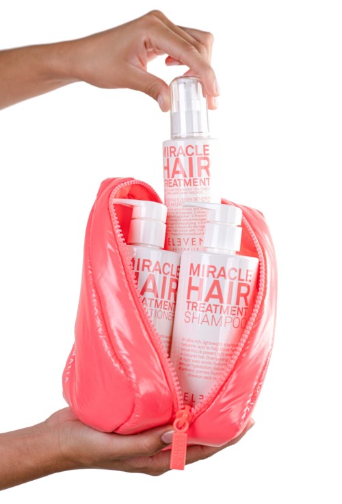 Hand placing a shampoo bottle into a pink cosmetic bag, with two other bottles visible inside.