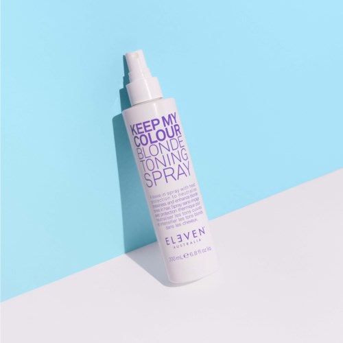 Eine weiße Sprühflasche mit lila Text, beschriftet 'Keep My Colour Blonde Toning Spray,' vor blau-weißem Hintergrund.