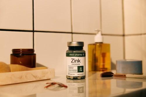 A bottle of zinc supplement on a bathroom counter with soap, jars, and a pump bottle nearby.