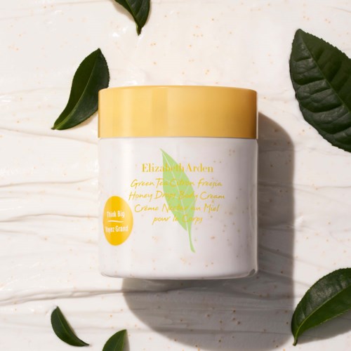 A white jar with a yellow lid, labeled as Elizabeth Arden Green Tea Citrine aroma cream, on a light surface with green leaves.