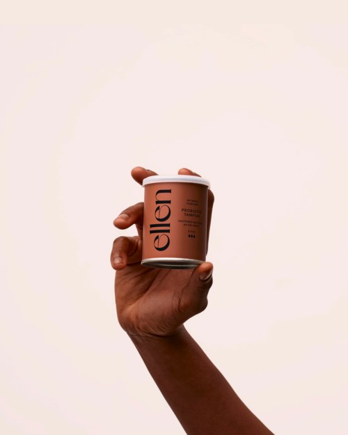 Eine Hand hält eine pinke Dose mit schwarzem Text, der 'Ellen' sagt, vor einem schlichten Hintergrund.