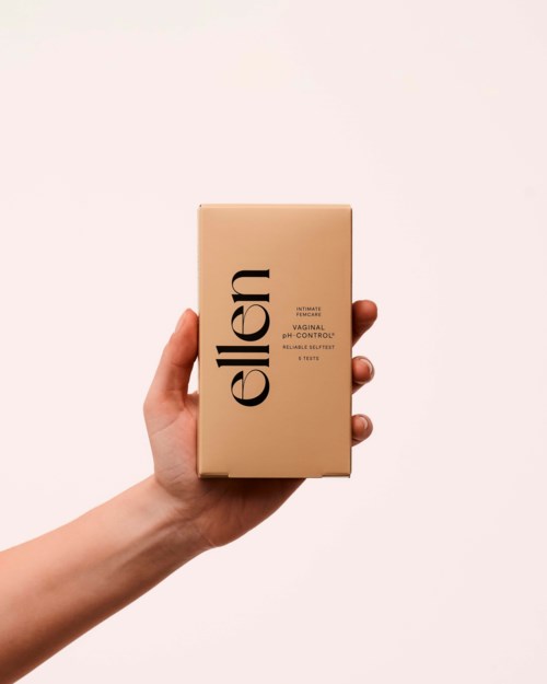 En hand håller en beige låda märkt 'ellen' med mindre text, mot en neutral bakgrund.
