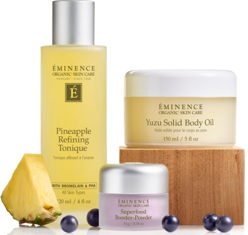 Three skincare products, pineapple slice, and blueberries arranged neatly, with a small platform and wooden block.