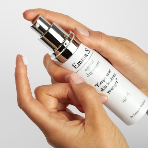 En hand applicerar kräm från en vit pumpflaska märkt för anti-aging hudvård. Bakgrunden är enkel och neutral.