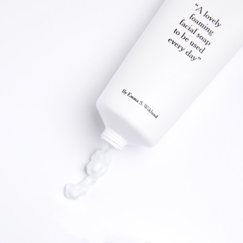 A white tube of foaming facial soap labeled 'A lovely foaming facial soap to be used every day' with some foam coming out.