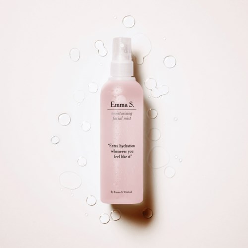 Pink facial mist spray bottle with water droplets around it on a white background.