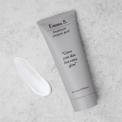 Een grijze tube met Emma S. behandeling enzympeel en slogan over stralende huid. Een dot crème ligt ernaast.