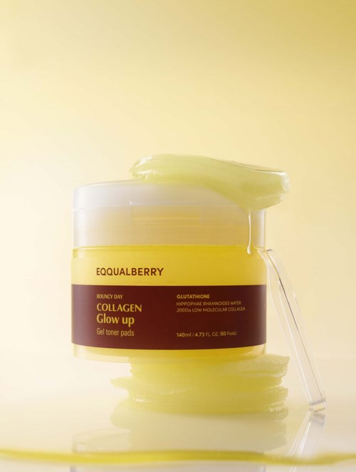 Een gele pot met collagen glow-up gel toner pads, met wat gel erboven en een lepel die op de pot leunt.