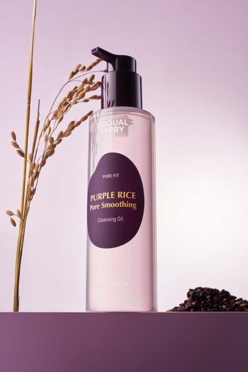 Eine klare Flasche Reinigungsöl mit der Bezeichnung 'Purple Rice Pure Smoothing' und getrocknetem Reis und Bohnen drumherum.