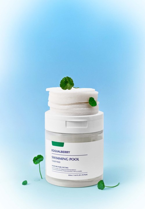 Een witte container met een label, omringd door groene bladeren en geplaatst tegen een blauwe achtergrond.