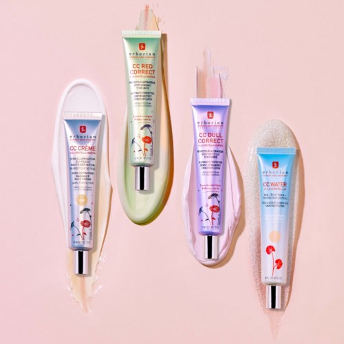 Four tubes of skincare products arranged on a pink background, each with different label colors: white, green, purple, and blue.