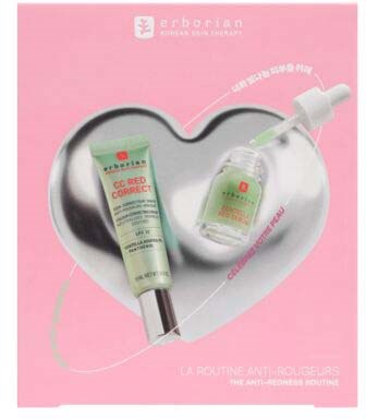 A skincare set with a green tube, a small dropper bottle, and a spatula on pink background, inside a heart-shaped dish.