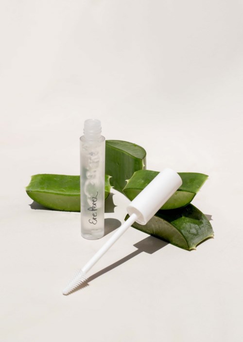 Een heldere fles en een witte pipet met aloë vera bladeren erachter. De opstelling ziet er schoon en eenvoudig uit.