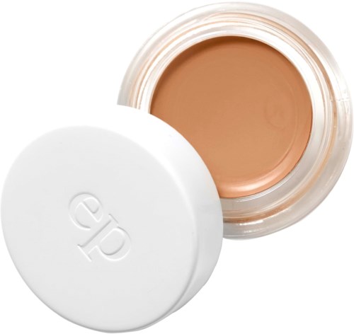 Ett glas med beige kräm eller foundation och en vit lock med en logga. Glaset är öppet och visar produkten inuti.