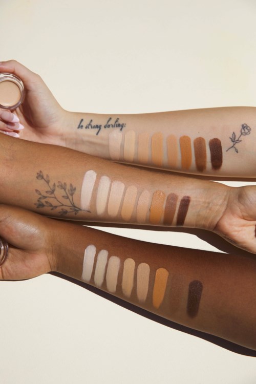Tre armar med olika hudtoner visar makeupprov och tatueringar, inklusive blommor, text och linjer.