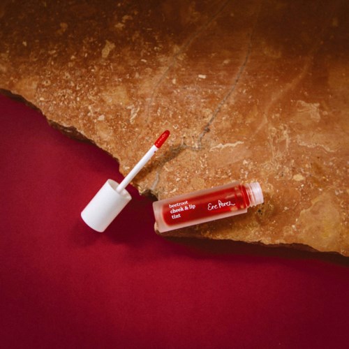 Lippenbalsemtube met applicator, op een ruwe stenen ondergrond met rode achtergrond.
