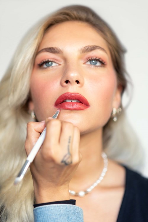Eine Frau bekommt von einem Make-up-Künstler Lippen mit Lippenstift betont, Fokus auf Gesicht und Schmuck.