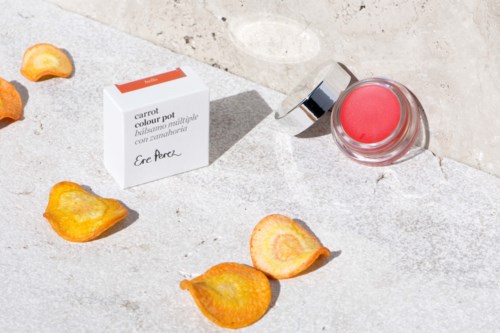 Kleine potje met roze crème, witte doos met gezichtscrème en oranje bloemblaadjes op een grijze ondergrond.