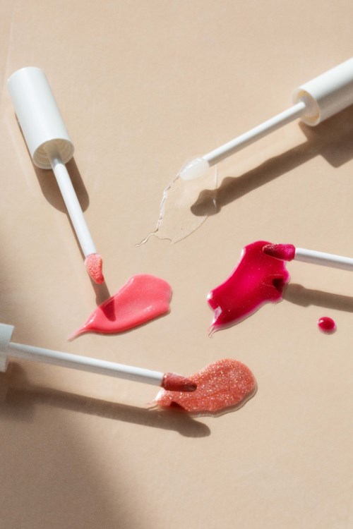 Vier lipgloss- of lipstickapplicators met verschillende tinten op een beige oppervlak.
