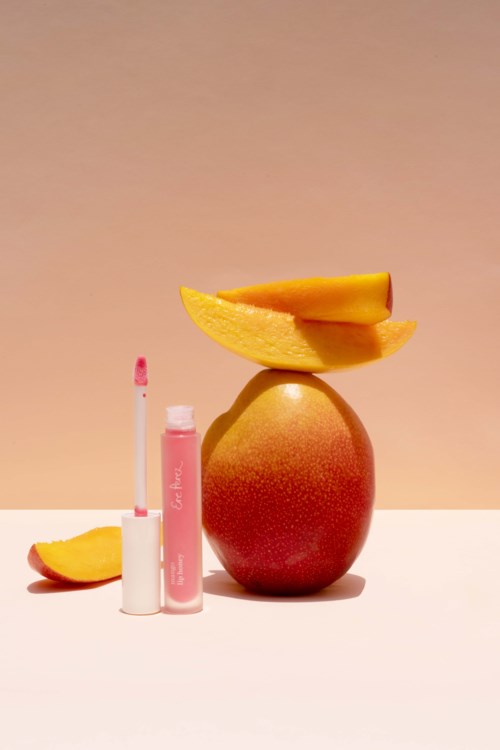 En mango balanseras på ett rött äpple med skivad mango på toppen. Läppglans och en liten mangobit finns i närheten.