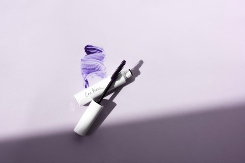 A mascara tube and brush with purple and black smudges on a light background.