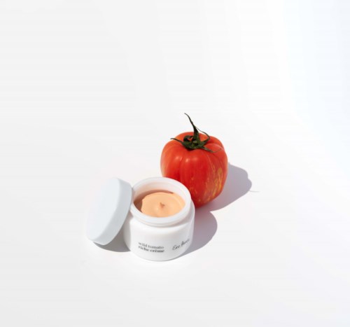 Een rijpe tomaat en een witte pot met crème op een witte achtergrond.