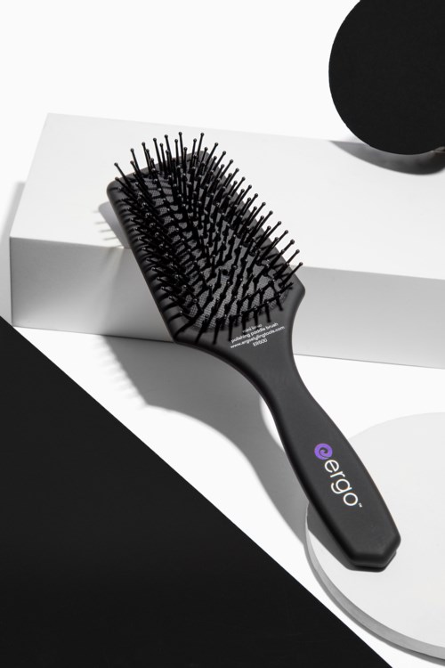 Eine schwarze Haarbürste mit Borsten auf einer weißen Box vor schwarzem Hintergrund.