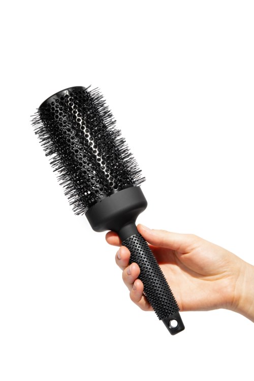 Eine Hand hält eine runde Haarbürste mit Borsten und schwarzem Griff.