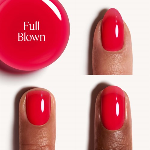 A red nail polish bottle beside three fingers with painted red nails.