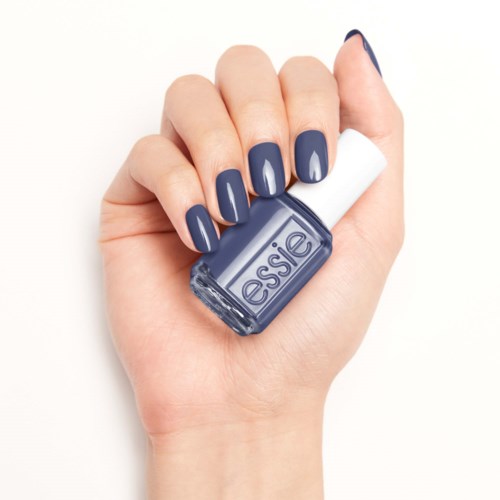 En hand med blåmålade naglar håller en liten flaska nagellack från Essie.