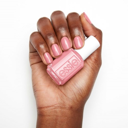 En hand håller nagellack i rosa märkt "essie" med matchande manikyr.