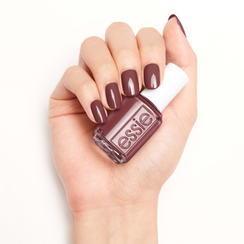 En hand med mörkröd nagellack håller en flaska Essie nagellack.