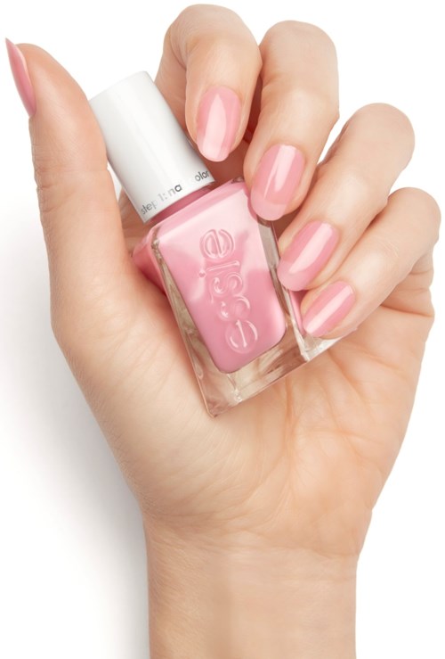 En hand med fint målade rosa naglar håller en liten rosa flaska nagellack.