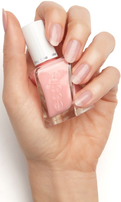 En hand håller en rosa nagellackflaska med vit kork, visar välskötta naglar.