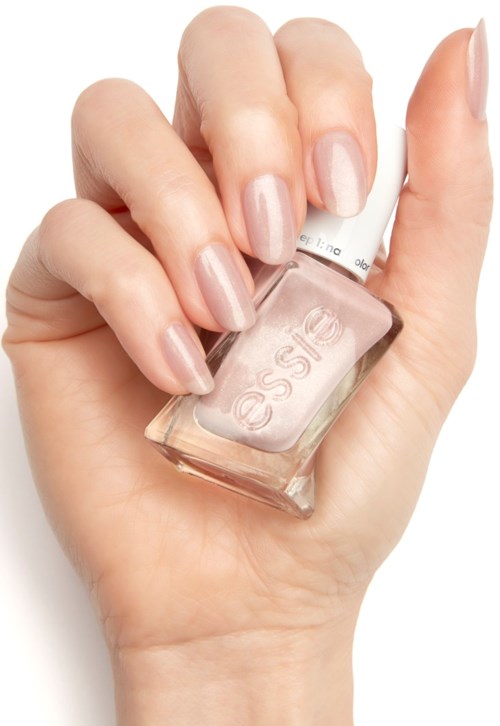 En hand med ljusrosa nagellack håller en klar Essie nagellackflaska mot en vit bakgrund.