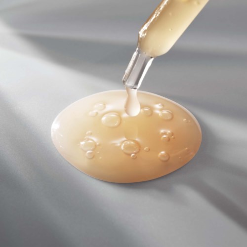 Een pipet druppelt een witte vloeistof op een glad oppervlak, waardoor kleine bellen en een dunne film ontstaan.
