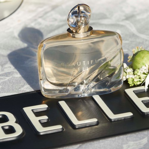Een parfumfles op een oppervlak met bloemen en het woord 'BELLE'.