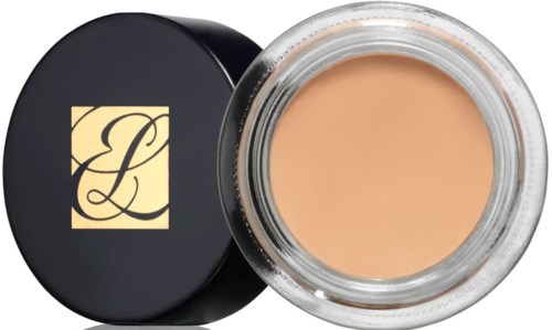 Een kleine ronde container met beige make-up en een zwarte deksel met een gouden logo.