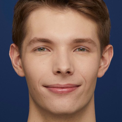 Een jonge man met lichte huid en kort bruin haar die glimlacht tegen een donkerblauwe achtergrond.