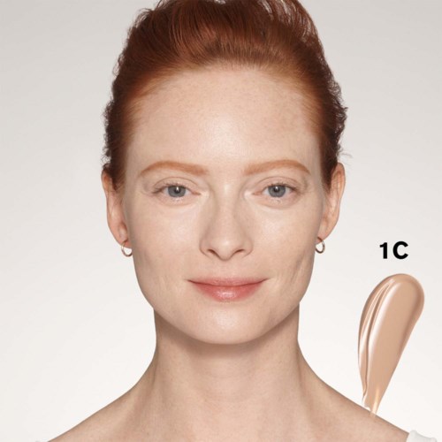 Een vrouw met rood haar en een lichte huid heeft een kleine hoeveelheid make-up gemarkeerd 1c op haar wang.