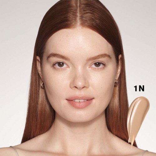 Een vrouw met recht, rood haar en minimale make-up. Ze heeft een neutrale uitdrukking en draagt oorbellen.