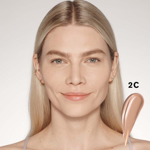 Eine Frau mit langem, blondem Haar, die sanft lächelt. Neben ihrer Schulter ist ein Kosmetikprodukt mit der Bezeichnung '2C'.