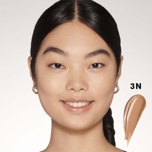 Een vrouw met zwart haar glimlacht, met een 3N make-up proef op haar wang.