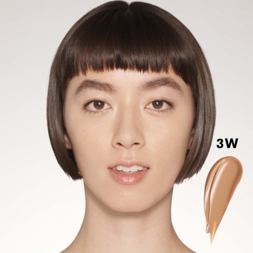Een vrouw met kort haar toont een proef van beige makeup of foundation met de aanduiding 3W.