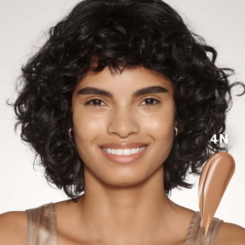 Een vrouw met krullend haar en oorbellen glimlacht naar de camera, draag een bruin mouwloos topje.