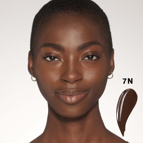 Een portret van een vrouw met natuurlijke huid, kort haar, zachte glimlach, met een lippenstiftlabel 7N.