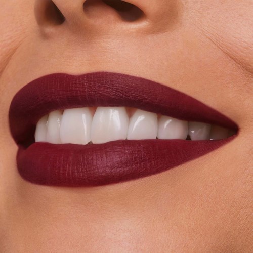 Close-up van iemands mond met witte tanden en donkerrode lippenstift, gedeeltelijk open in een glimlach.